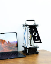 3D printer on a desk next to a laptop with a scenic display.