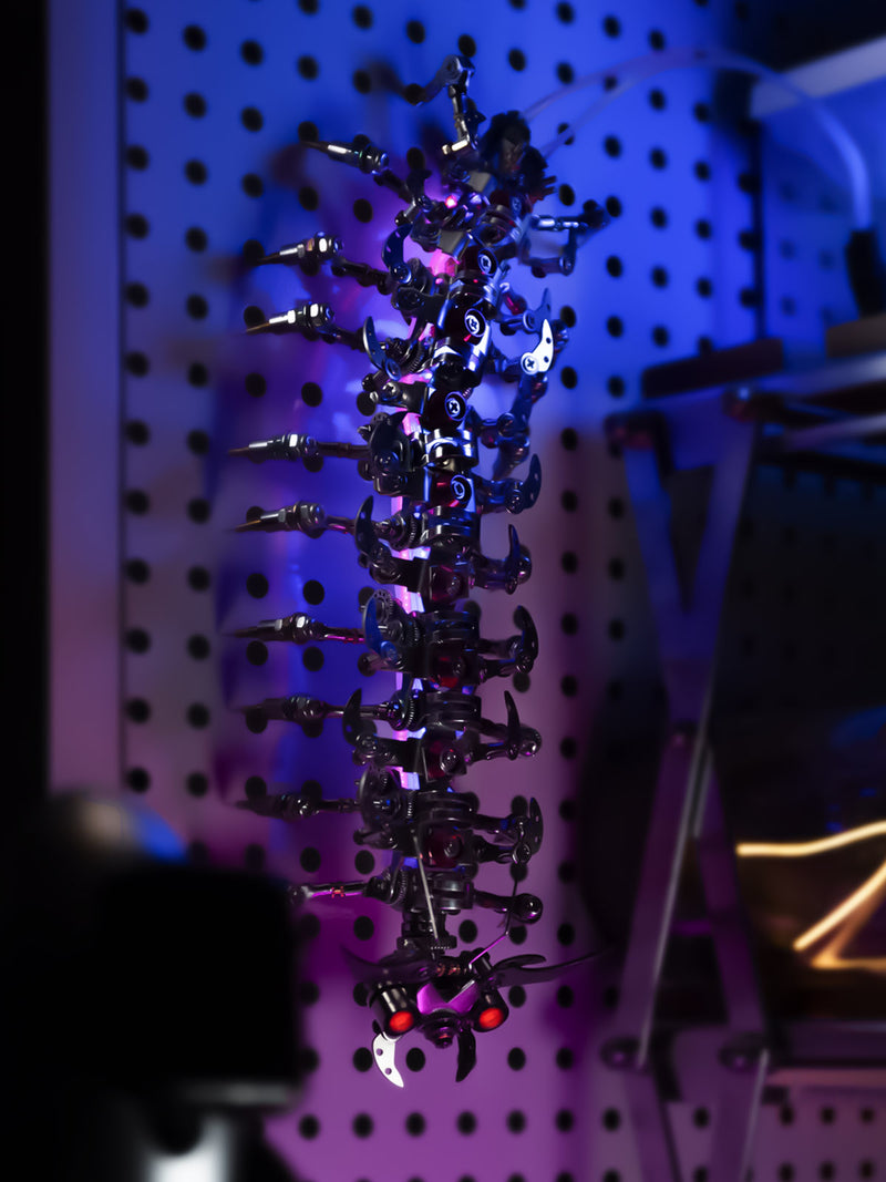 A biomechanical sculpture featuring a vertical array of mechanical parts with a futuristic aesthetic, illuminated by colored lights.