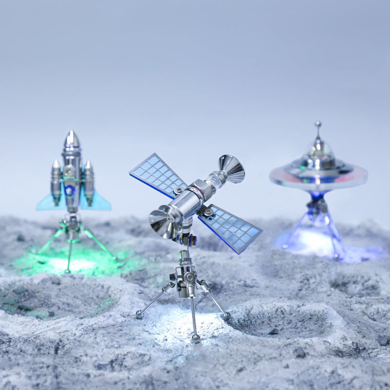 Toy models of a space station, spaceship, and flying saucer on a moon-like surface with a gray background.