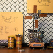 A steampunk-style mechanical sculpture or model on a wooden base, displayed on a tabletop with metal cans, gears, and blueprint posters against a diamond-pattern backdrop.