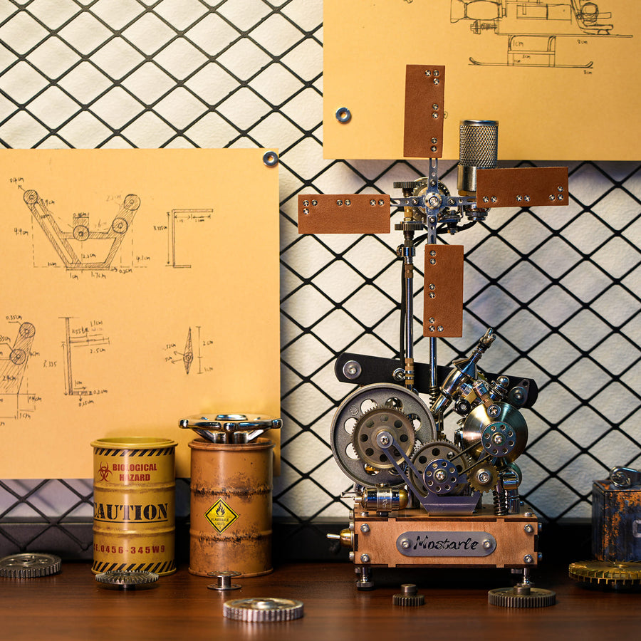 A steampunk-style mechanical sculpture or model on a wooden base, displayed on a tabletop with metal cans, gears, and blueprint posters against a diamond-pattern backdrop.