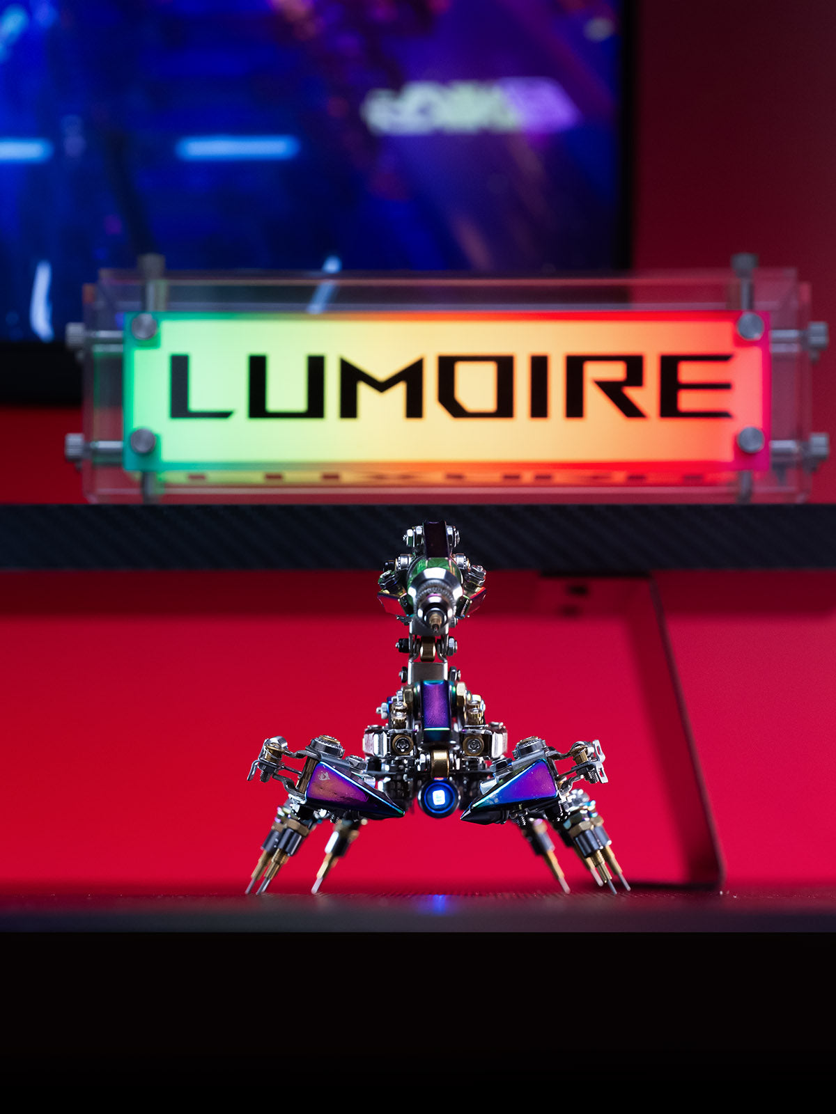 Metallic robot-like sculpture on a red platform with 'LUMOIRE' branding in the background.