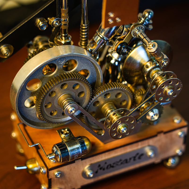 Close-up of a steampunk mechanical model with brass gears, metal rods, and a wooden base featuring the name 'Klossart' on a metal plate, set against a dark wooden background.