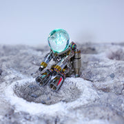 Small robot with a glowing blue sphere on a textured surface