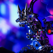 Close-up of a metallic, intricate object with spikes against a blurred colorful background