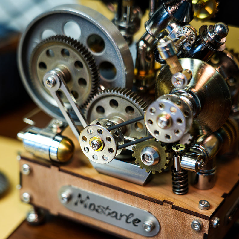 Close-up of a steampunk mechanical model with interlocking metal gears, springs, and brass-toned parts mounted on a wooden base. A metal plate on the front reads 'Mostarle'.